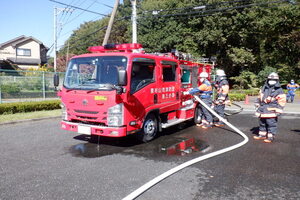 写真：赤い」消防団車両にホースをつないでいる様子