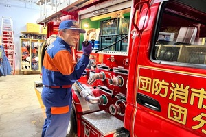 写真：消防車の横に立ち無線を手にしている隊員